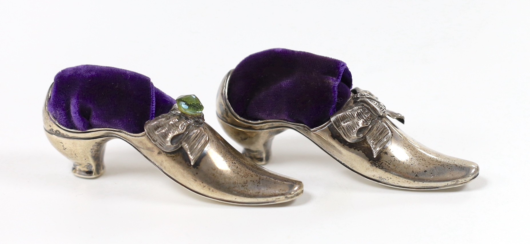 Two similar late Victorian novelty silver mounted pin cushions, modelled as shoes, one set with later green stone, Adie & Lovekin, Birmingham, 1890, length 83mm (later cushions).